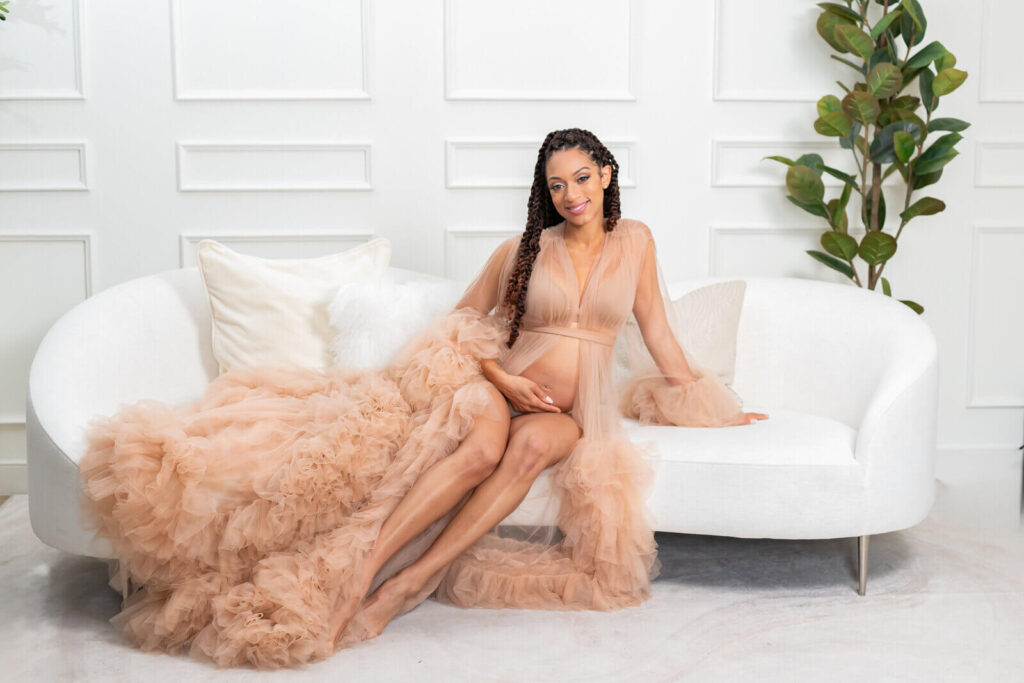 Goddess Maternity photoshoot beautiful black woman sitting on white couch in brown goddess dress